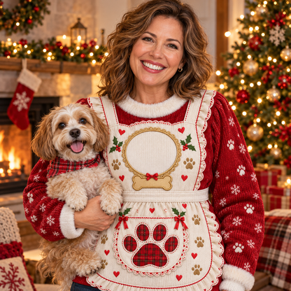 Woman in a Mrs. Claus apron ugly Christmas sweater holding her dog